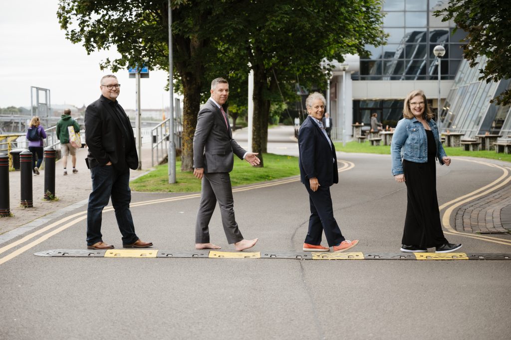 The four hosts crossing the street and smiling, looking like the famous Beatles album cover for Abbey Road.