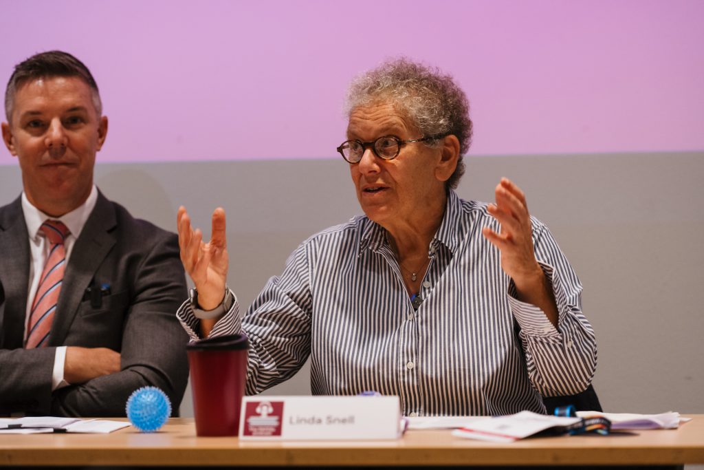 Panel discussion in progress with an engaged speaker gesturing while making a point, as a co-panelist listens attentively.